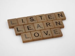 Wooden Scrabble tiles arranged to spell 'Listen, Learn, Love' on a white background.
